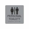 Silvergrå och svart skylt för personaltoalett med piktogram av en kvinna och en man åtskilda av ett lodrätt streck, texten personal toalett står under symbolen och punktskrift längst ned