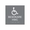 Grå och vit toalettskylt för besökare hwc med piktogram av en rullstol, texten besökare hwc står under symbolen och punktskrift längst ned