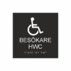Svart och vit toalettskylt för besökare hwc med piktogram av en rullstol, texten besökare hwc står under symbolen och punktskrift längst ned