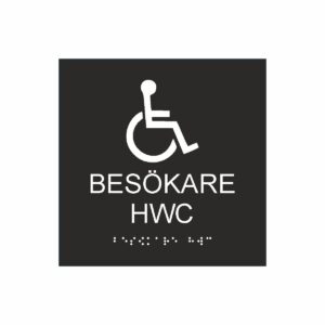 Svart och vit toalettskylt för besökare hwc med piktogram av en rullstol, texten besökare hwc står under symbolen och punktskrift längst ned
