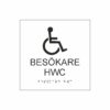 Vit och svart toalettskylt för besökare hwc med piktogram av en rullstol, texten besökare hwc  står under symbolen och punktskrift längst ned